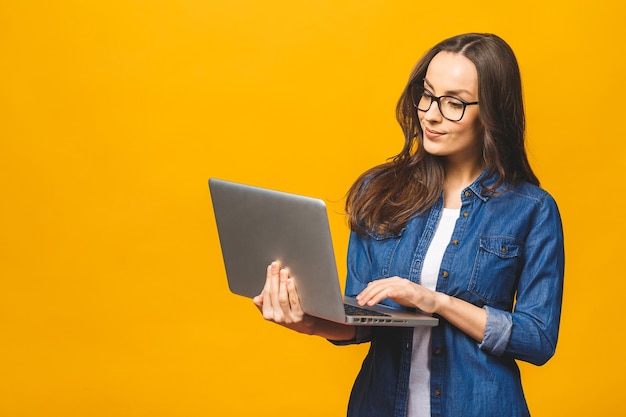 Giovane donna sorridente felice in abiti casual tenendo il computer portatile e l'invio di posta elettronica