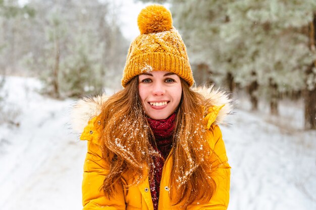 Giovane donna sorridente felice in giacca gialla nella foresta di inverno nevoso