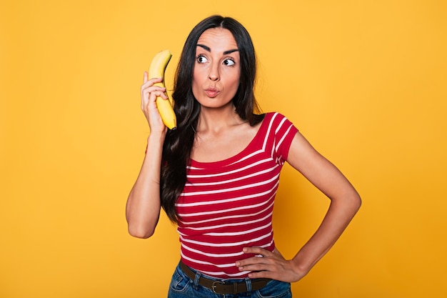 Giovane donna sorridente in abiti casual che si divertono con una banana su sfondo arancione