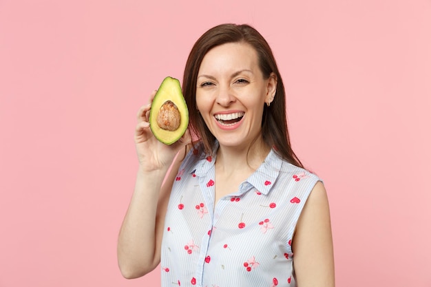 Giovane donna sorridente in abiti estivi che tiene metà del frutto di avocado verde maturo fresco isolato su sfondo rosa pastello in studio. Lo stile di vita vivido delle persone si rilassa il concetto di vacanza. Mock up spazio di copia.