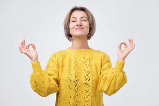 Giovane donna sorridente in maglione giallo che medita tenendosi per mano nel gesto di yoga