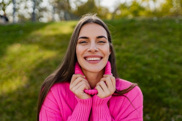 Giovane donna sorridente in maglione rosa che cammina nel parco verde