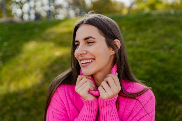 Giovane donna sorridente in maglione rosa che cammina nel parco verde