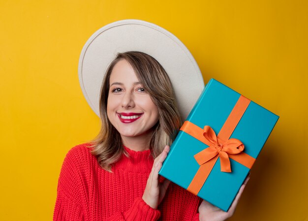 Giovane donna sorridente in maglione rosso con scatola regalo