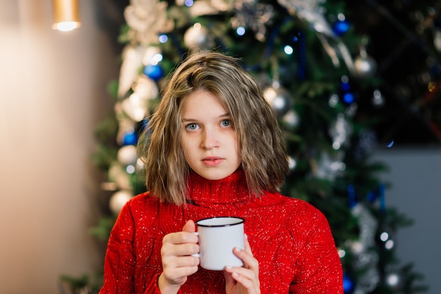 Giovane donna sorridente in maglione, vacanze invernali in interni domestici decorati con albero di Natale.