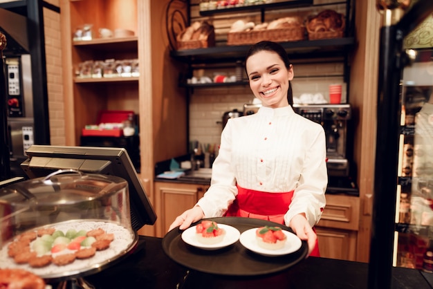 Giovane donna sorridente in piedi con le torte in forno.