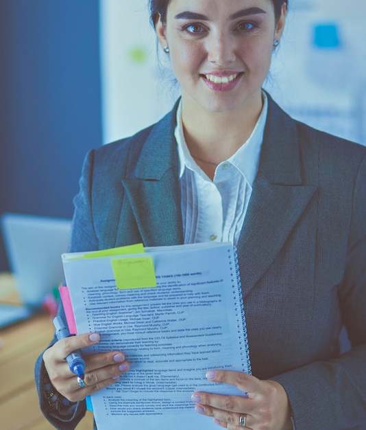 Giovane donna sorridente in piedi e in possesso di un libro in ufficio