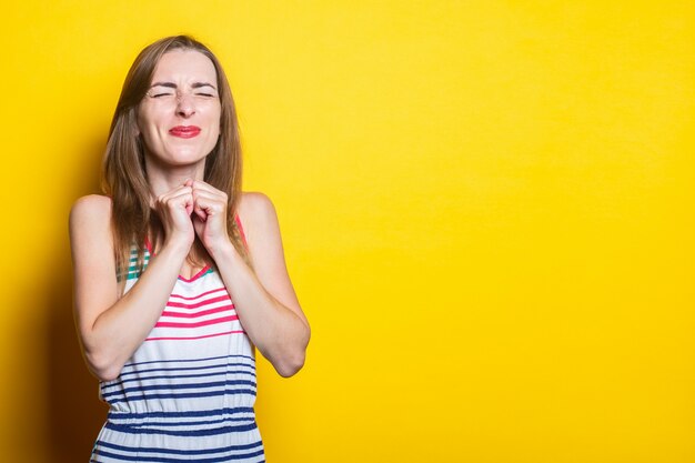 Giovane donna sorridente in un abito a righe strabismo e tenendo i pugni su uno sfondo giallo