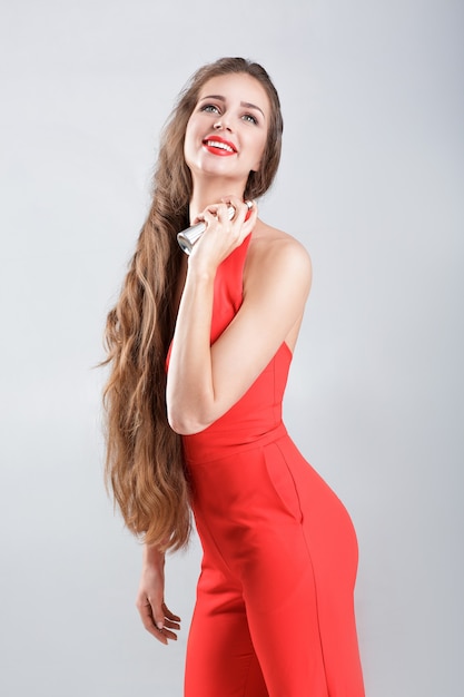 Giovane donna sorridente in vestito rosso che applica profumo sul suo collo