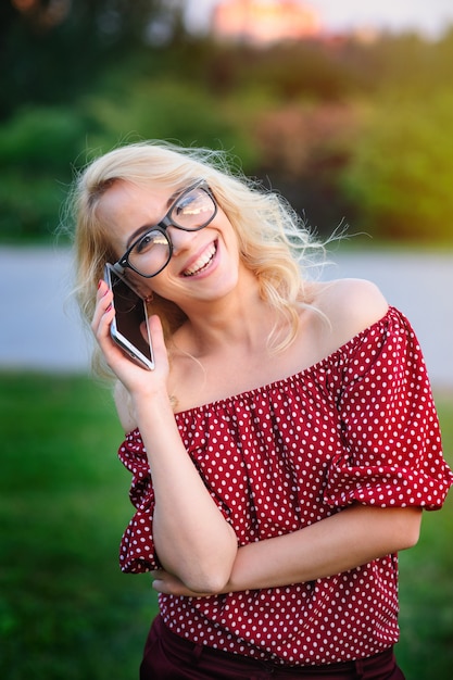 Giovane donna sorridente in vetri con il telefono all&#39;aperto