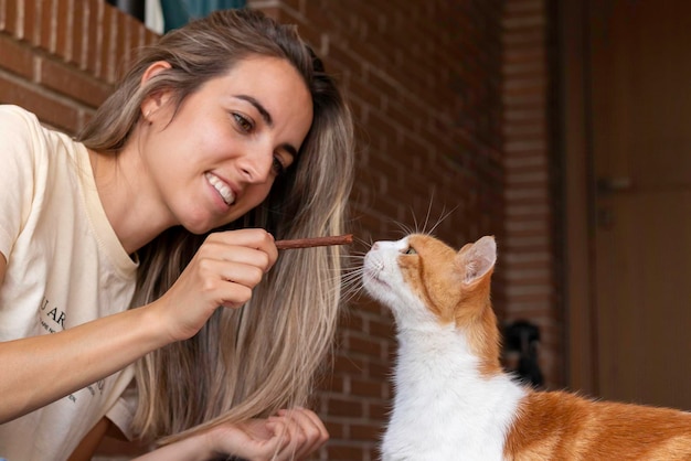 Giovane donna sorridente mentre educa il suo gatto con una sorpresa nel patio anteriore