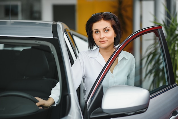 Giovane donna sorridente nella sua nuova auto in uno showroom