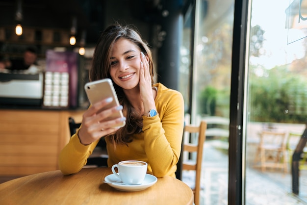 Giovane donna sorridente utilizzando smarphone nel caffè. Vista frontale.