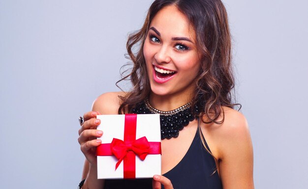 Giovane donna sorriso felice tenere la scatola regalo nelle mani isolato sullo sfondo grigio