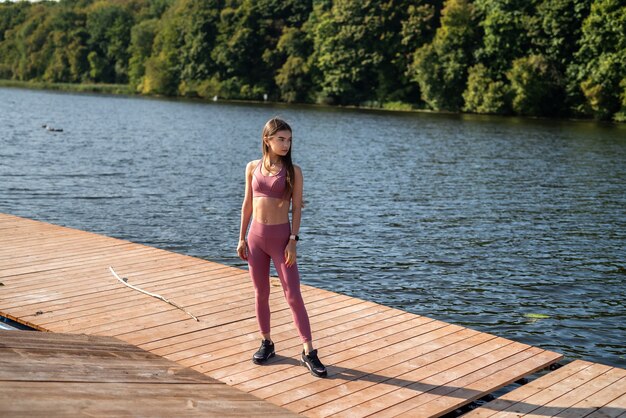 Giovane donna sottile che indossa abbigliamento sportivo riposo dopo l'esercizio mattutino vicino al lago