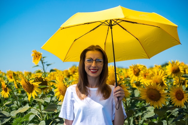 Giovane donna sotto l'ombrello giallo al campo di girasoli.