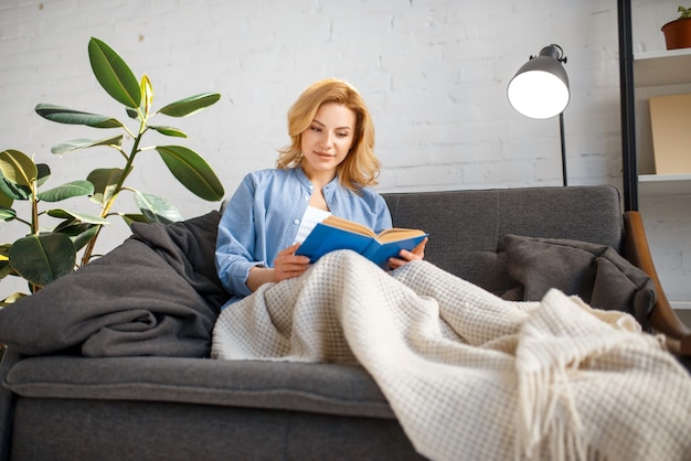 Giovane donna sotto un libro di lettura coperta sul divano