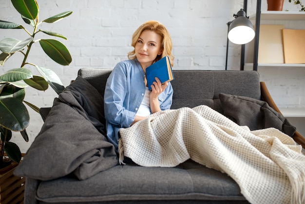 Giovane donna sotto un libro di lettura coperta sul divano