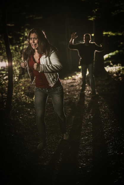 Giovane donna spaventata che corre attraverso la foresta di notte in abito bianco e scappa dall'uomo.