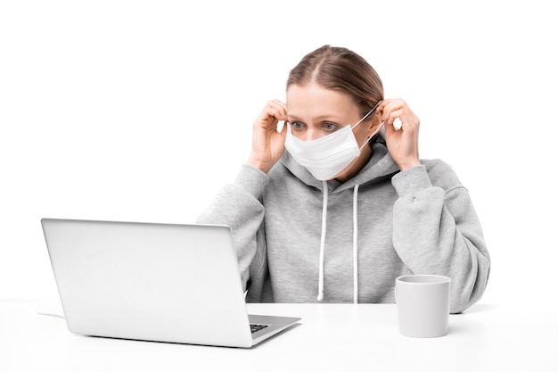Giovane donna spaventata dal coronavirus che regola la maschera e legge le notizie sul laptop
