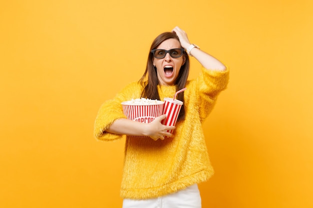 Giovane donna spaventata in occhiali 3d imax che urla aggrappandosi alla testa, guardando film, tenendo in mano popcorn, tazza di cola o soda isolato su sfondo giallo. Persone sincere emozioni nel cinema, nello stile di vita.