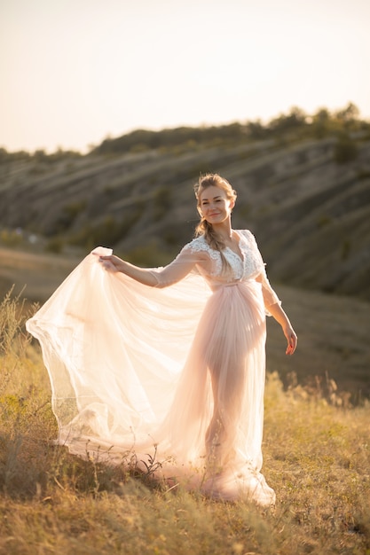 Giovane donna splendida in vestito rosa-aria che posa nel campo