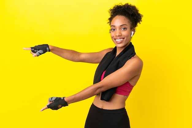 Giovane donna sportiva africana isolata su sfondo giallo che punta il dito di lato e presenta un prodotto