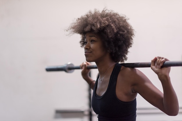 Giovane donna sportiva afroamericana carina nella sala fitness che solleva la barra vuota