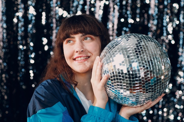 Giovane donna sportiva anni '80 e '90 stile anni '90 moda ragazza positiva alla festa in discoteca con palla da discoteca in mano