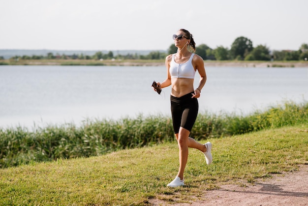 Giovane donna sportiva che corre nel parco vicino allo stagno in una calda giornata estiva