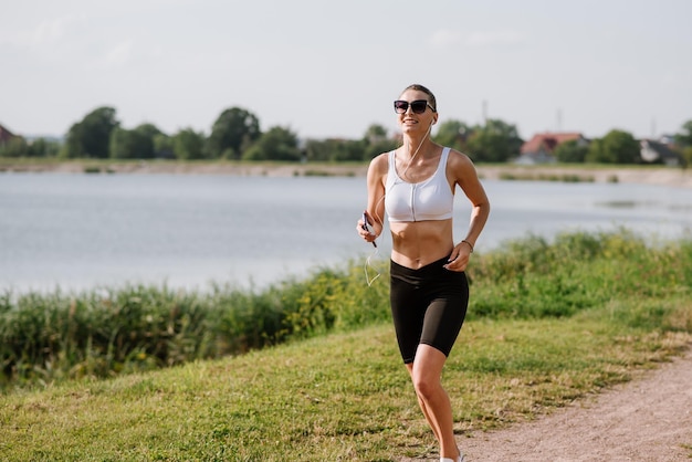 Giovane donna sportiva che corre nel parco vicino allo stagno in una calda giornata estiva