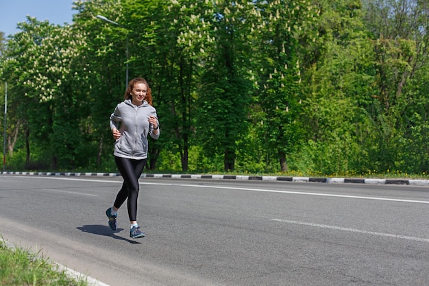 Giovane donna sportiva che corre su strada durante l'allenamento mattutino, copia spazio