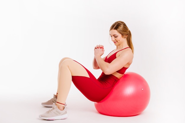 Giovane donna sportiva che fa esercizi con fitball su sfondo bianco