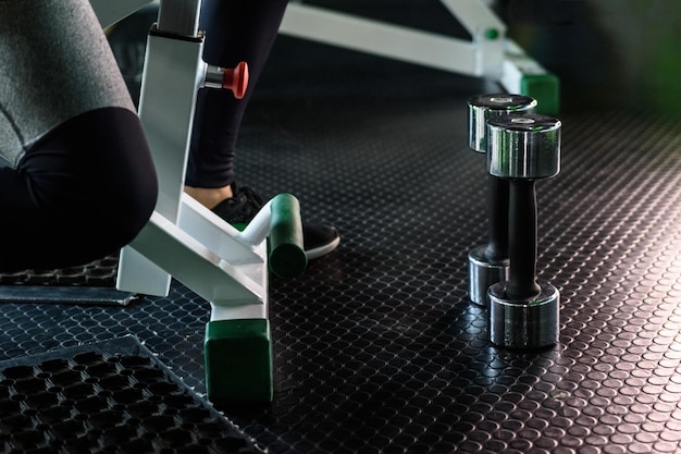 Giovane donna sportiva che fa esercizi con manubri seduti su una panchina in palestra. Fitness.