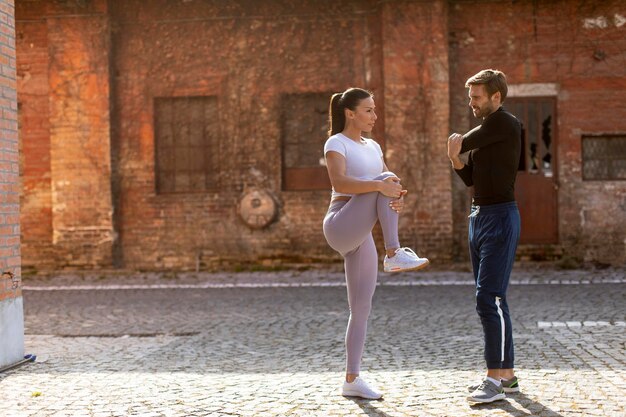 Giovane donna sportiva che fa esercizio di stretching dopo aver fatto jogging con il suo personal trainer