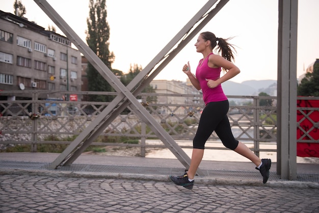 giovane donna sportiva che fa jogging attraverso il ponte al mattino soleggiato in città