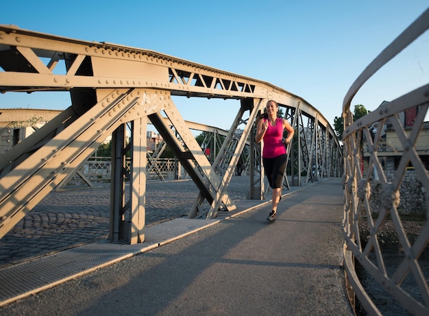 giovane donna sportiva che fa jogging attraverso il ponte al mattino soleggiato in città