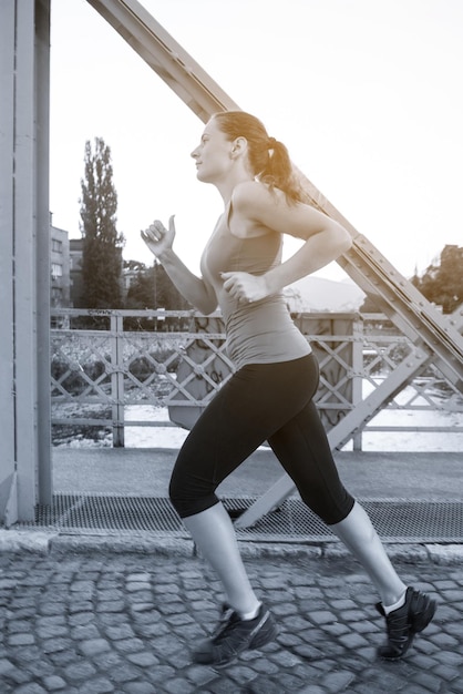 giovane donna sportiva che fa jogging attraverso il ponte al mattino soleggiato in città