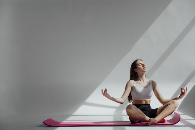 Giovane donna sportiva che fa pratica di yoga isolata su fondo bianco. Concetto di vita sana