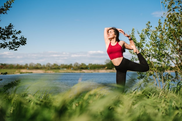 Giovane donna sportiva che pratica yoga all'aperto in riva al lago