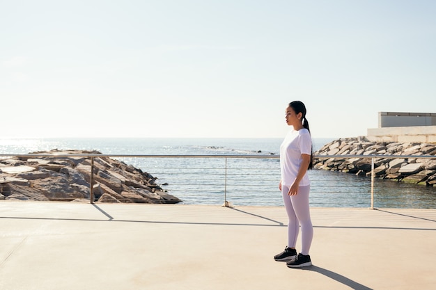 Giovane donna sportiva che si concentra sullo stare in piedi durante l'allenamento all'aperto, il concetto di sport e uno stile di vita attivo