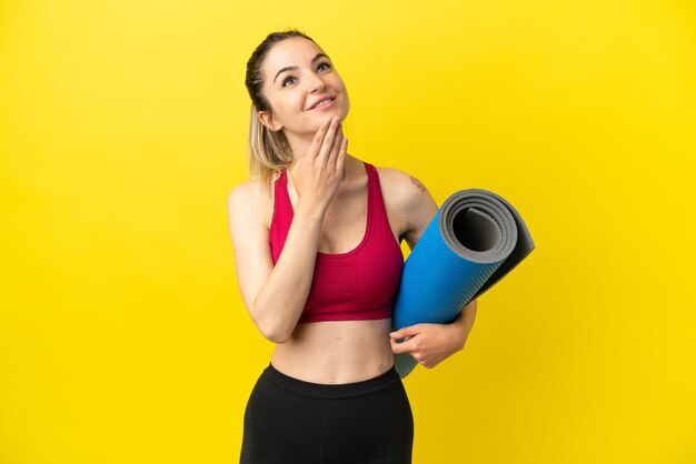 Giovane donna sportiva che va alle lezioni di yoga mentre tiene in mano un tappetino guardando in alto sorridendo