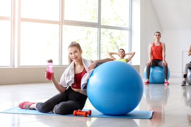 Giovane donna sportiva con acqua potabile fitball in palestra