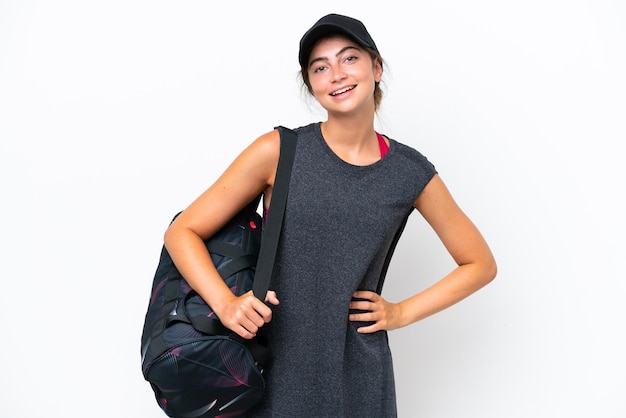 Giovane donna sportiva con borsa sportiva isolata su sfondo bianco in posa con le braccia all'anca e sorridente