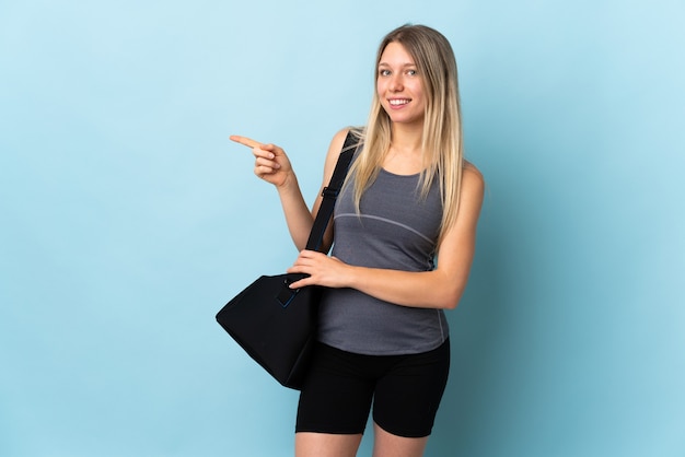 Giovane donna sportiva con borsa sportiva isolata sulla parete blu che indica il dito di lato
