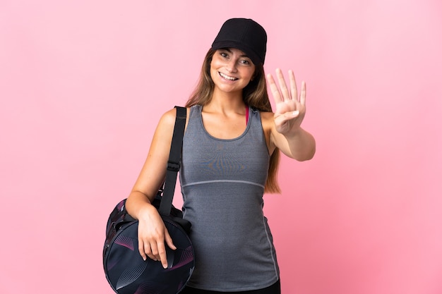 Giovane donna sportiva con borsa sportiva isolata sulla parete rosa felice e contando quattro con le dita