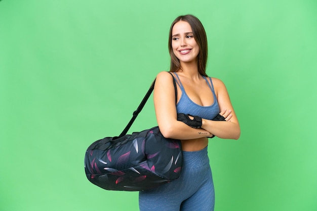 Giovane donna sportiva con borsa sportiva su sfondo chroma key isolato con le braccia incrociate e felice
