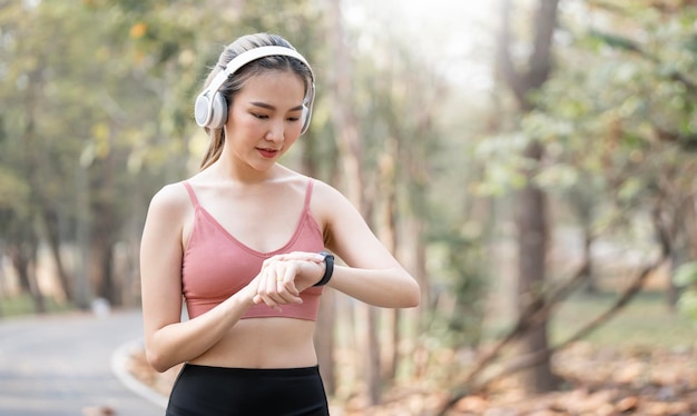 Giovane donna sportiva con cuffie wireless che utilizza smartwatch controlla il tracker attività durante l'esercizio all'aperto