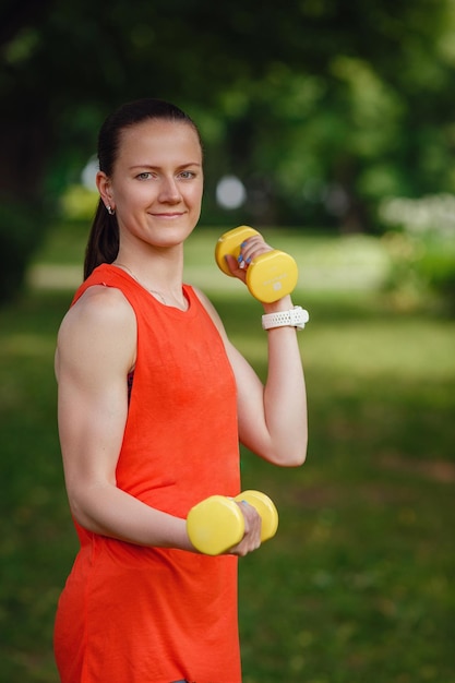 Giovane donna sportiva con manubri all'aperto Fare attività in forma e allenamento all'aperto sull'erba verde al parco Fitness sport e stile di vita sano