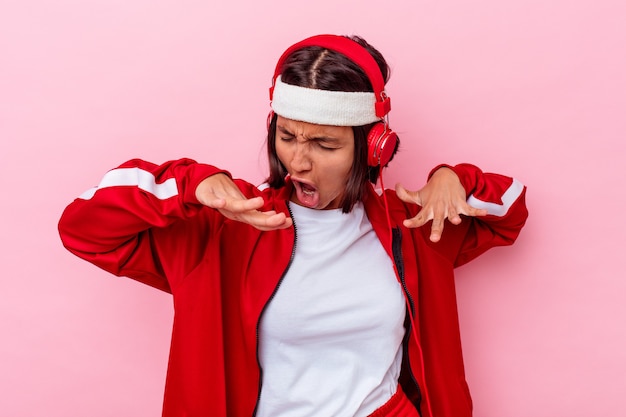 Giovane donna sportiva di razza mista ascoltando musica isolata su sfondo rosa